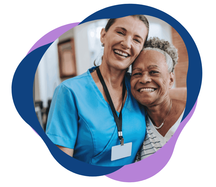 Nurse warmly embracing a happy elderly woman in a care setting.